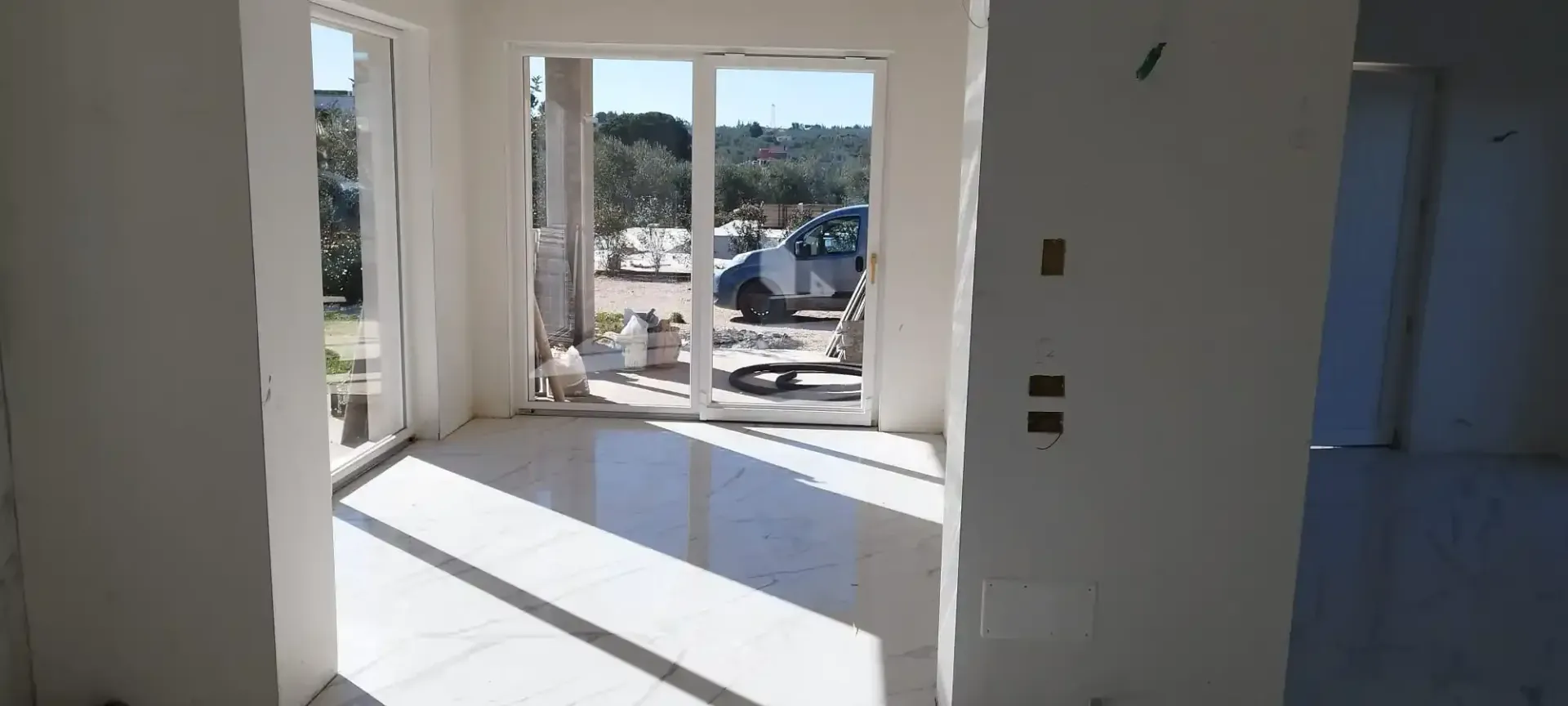 Stanza bianca e luminosa con grandi porte scorrevoli, luce solare e vista sul verde.