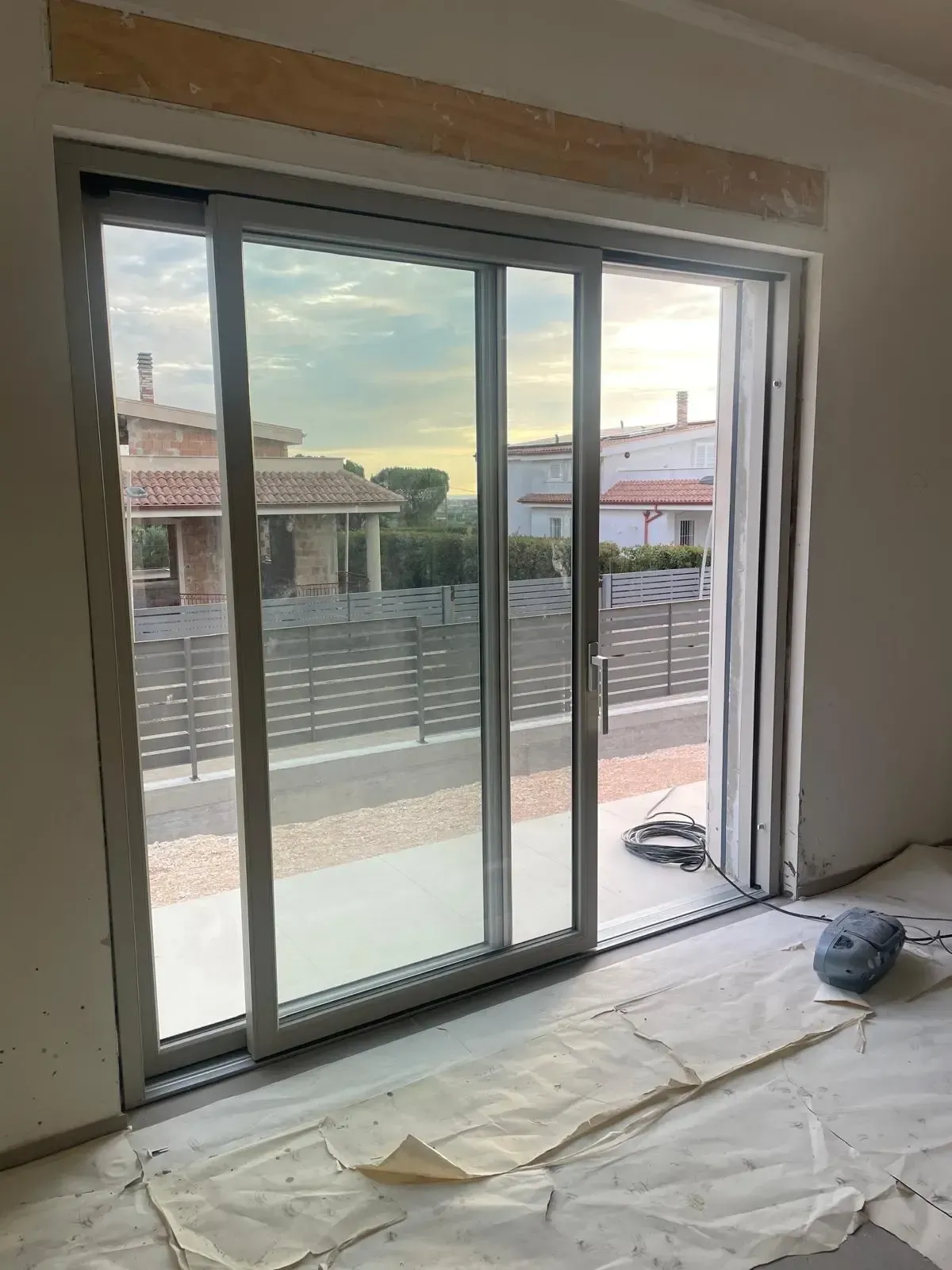 Porta scorrevole in vetro con vista su un patio e sulle case. Materiali da costruzione sul pavimento.