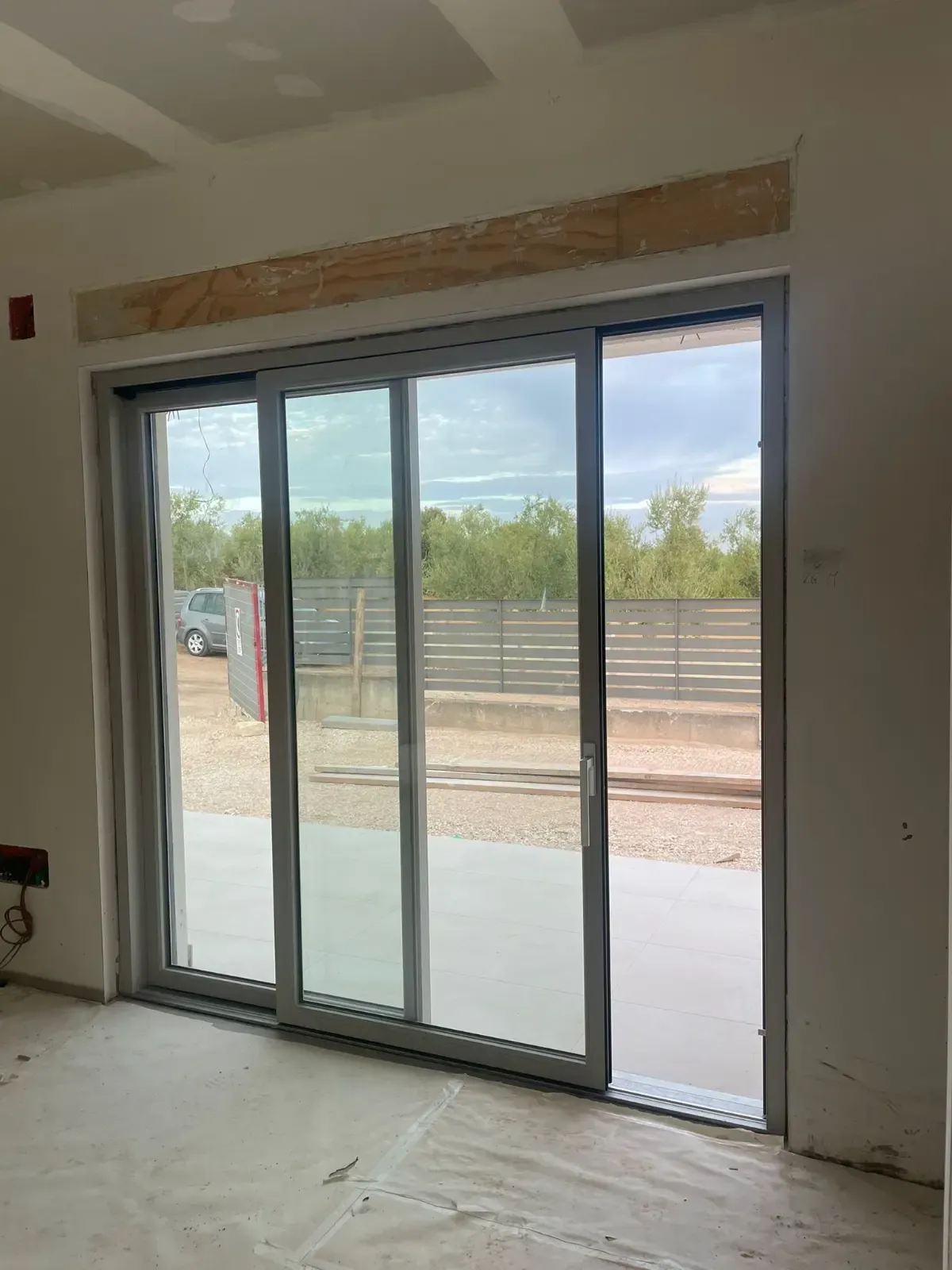 Porte scorrevoli in vetro con telaio grigio, interni grezzi. All'esterno recinzione e ghiaia.