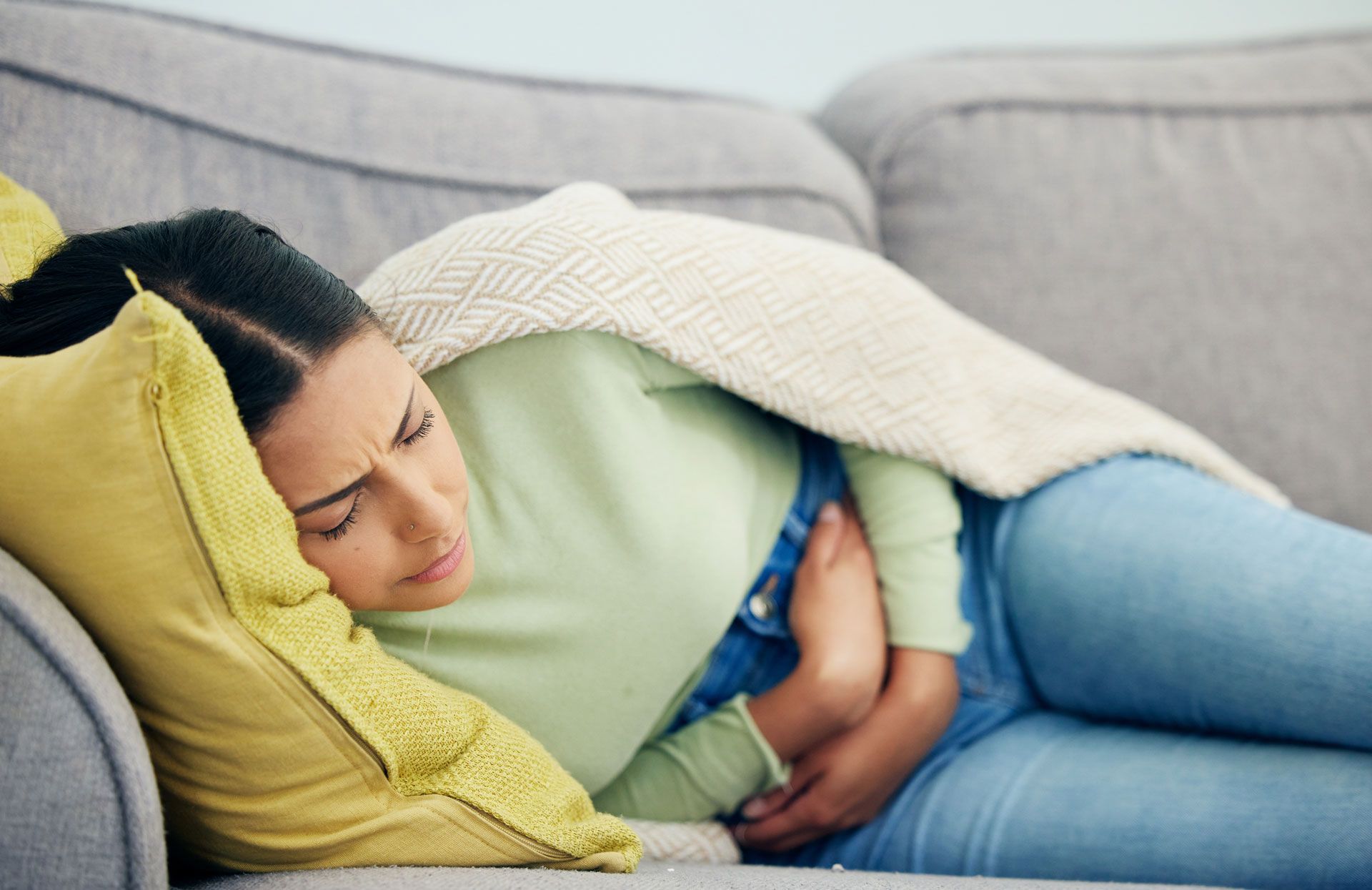 A woman is lying on a couch, experiencing menstrual pain, in Kennesaw.