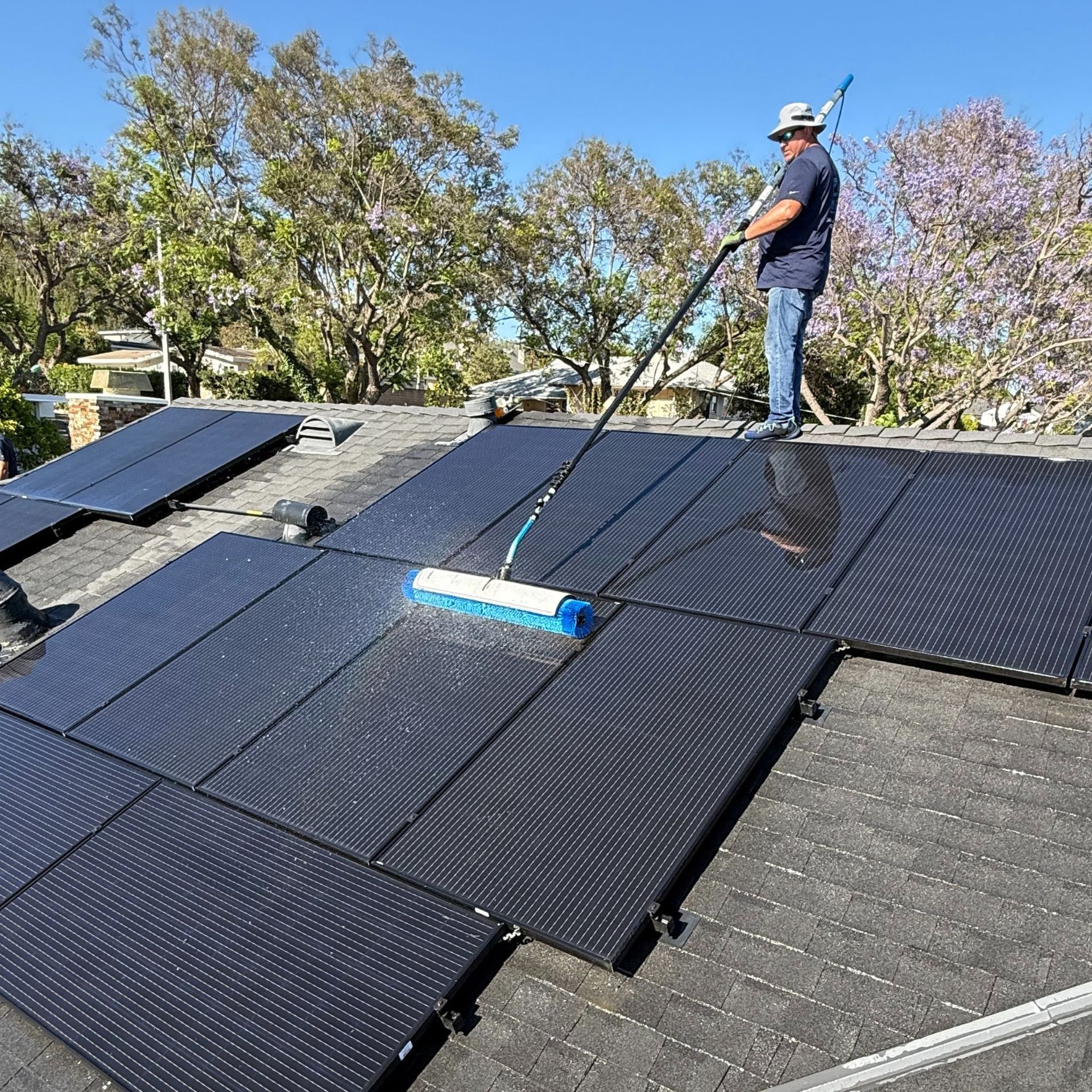 NFG Solar Panel Cleaning Company - A man is cleaning solar panels on a roof with a broom.