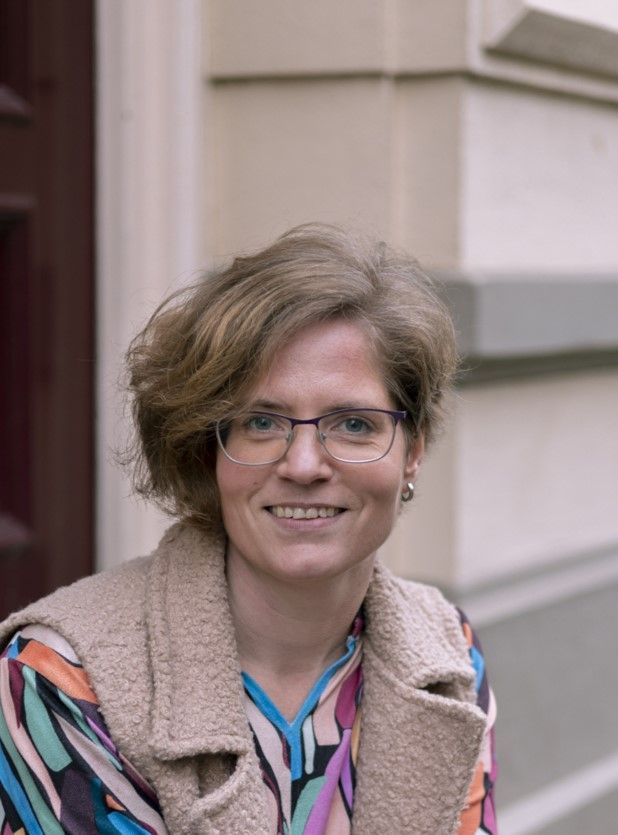 een vrouw met een bril en een shirt met luipaardprint lacht naar de camera