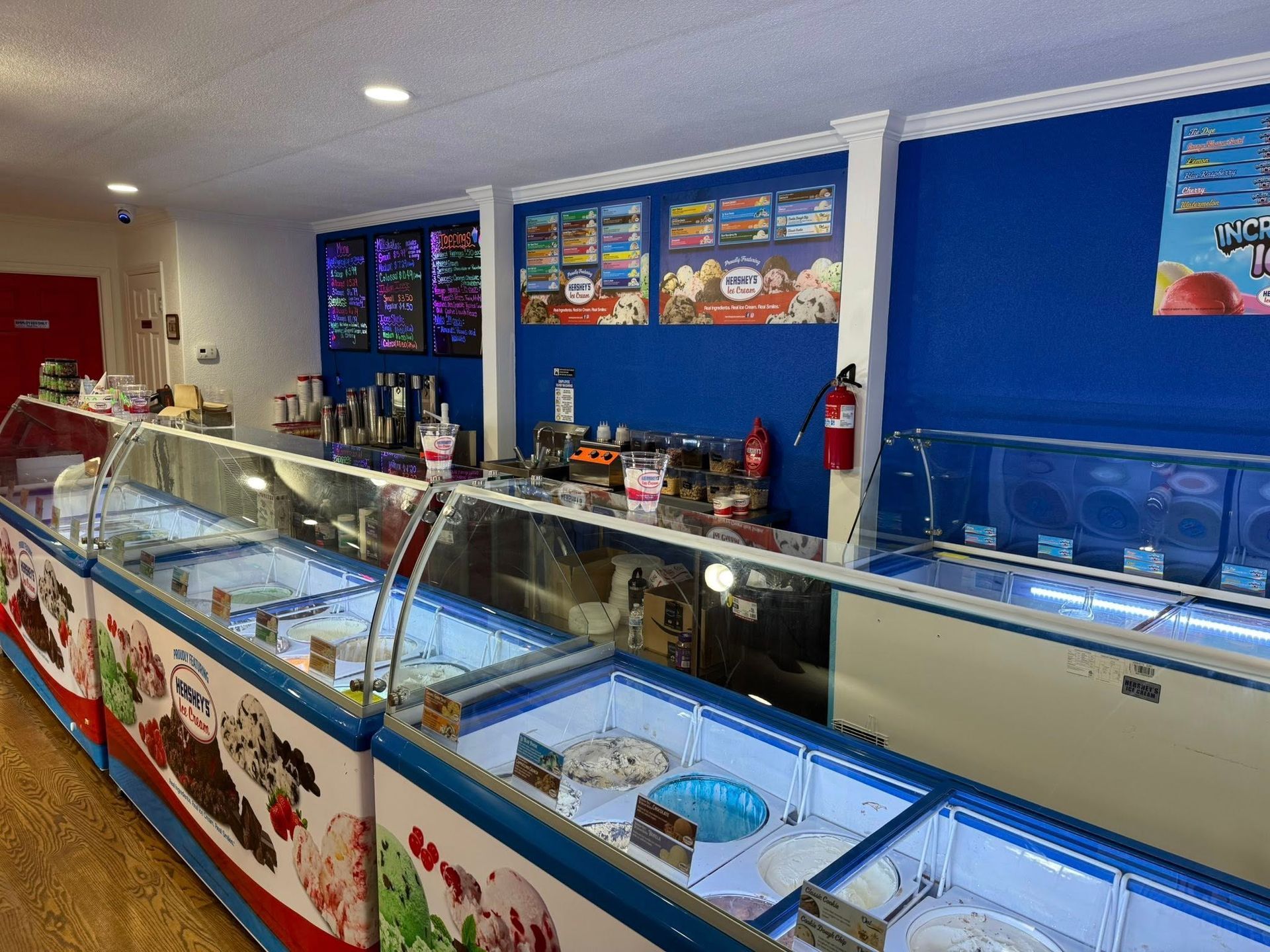 An ice cream parlor with rows of glass-topped freezer display cases against a blue wall with menu boards.