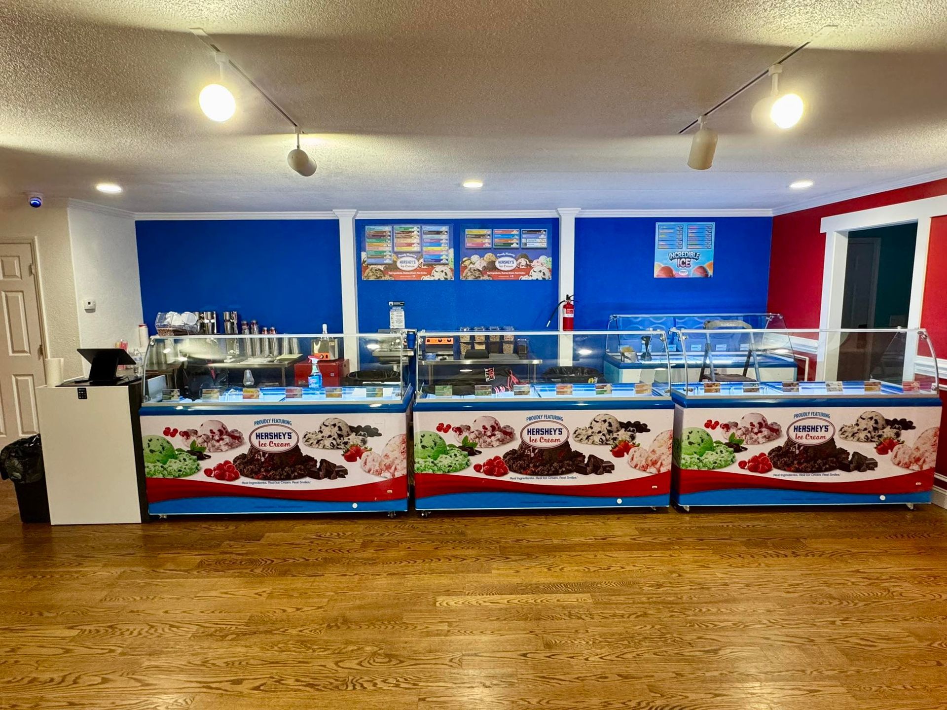 Three rows of ice cream display cases in a shop with blue walls and wood floors.