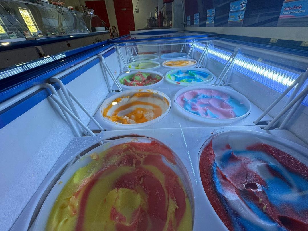 A brightly lit freezer display case filled with rows of tubs containing colorful, swirled ice cream flavors.
