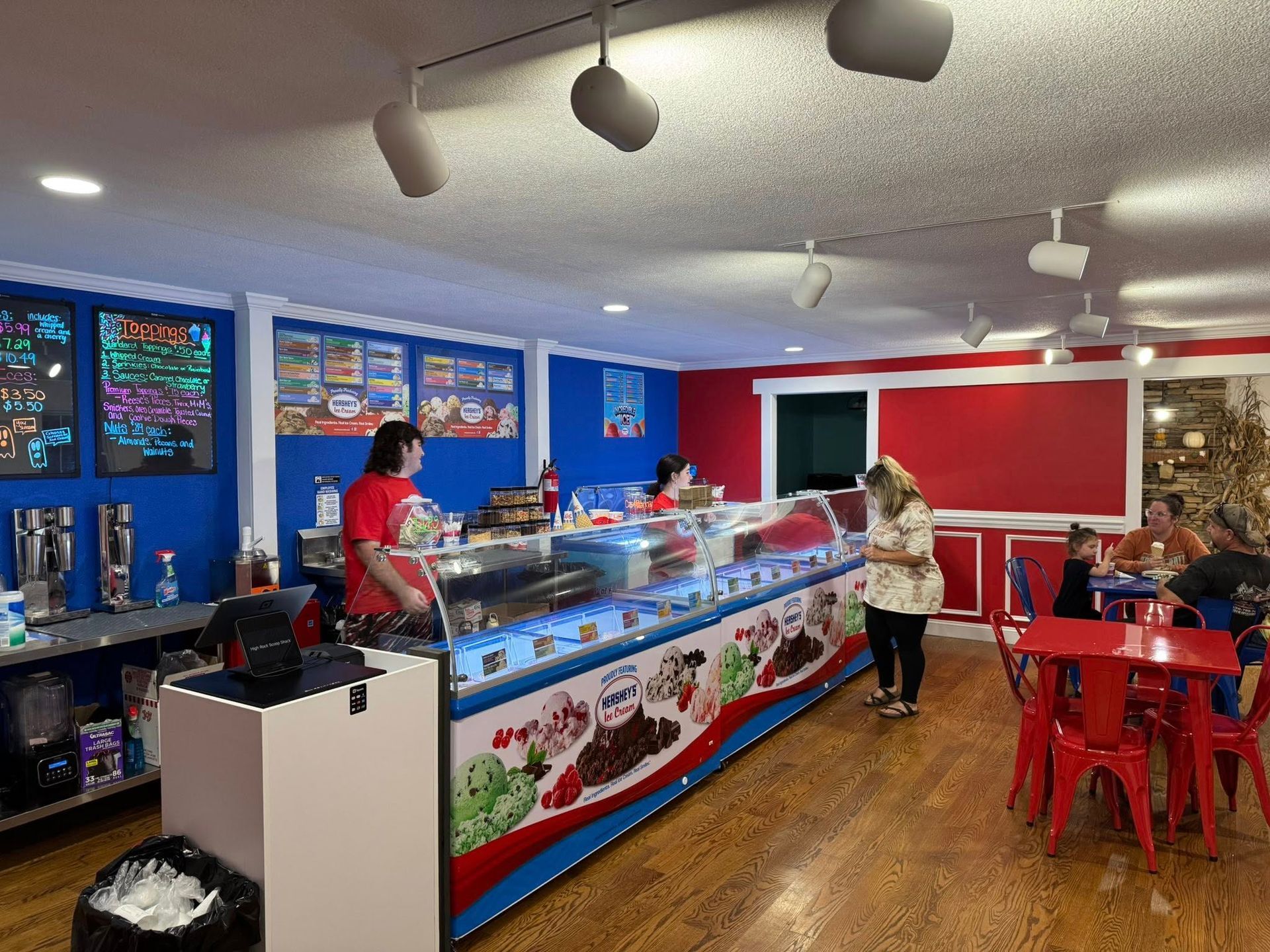 An ice cream parlor featuring a service counter, menu boards, staff, and customers seated at tables.
