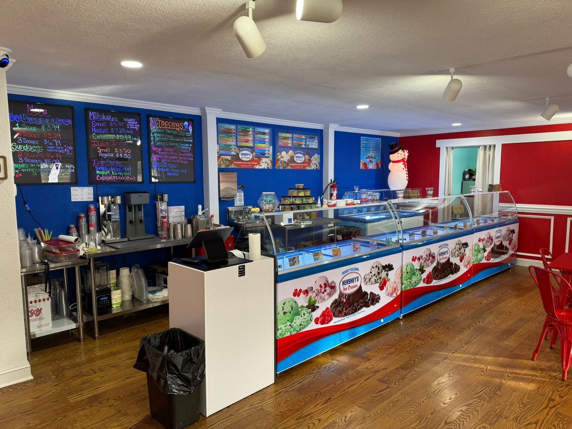An ice cream shop interior featuring a long, decorated serving counter with menu boards on a deep blue wall.