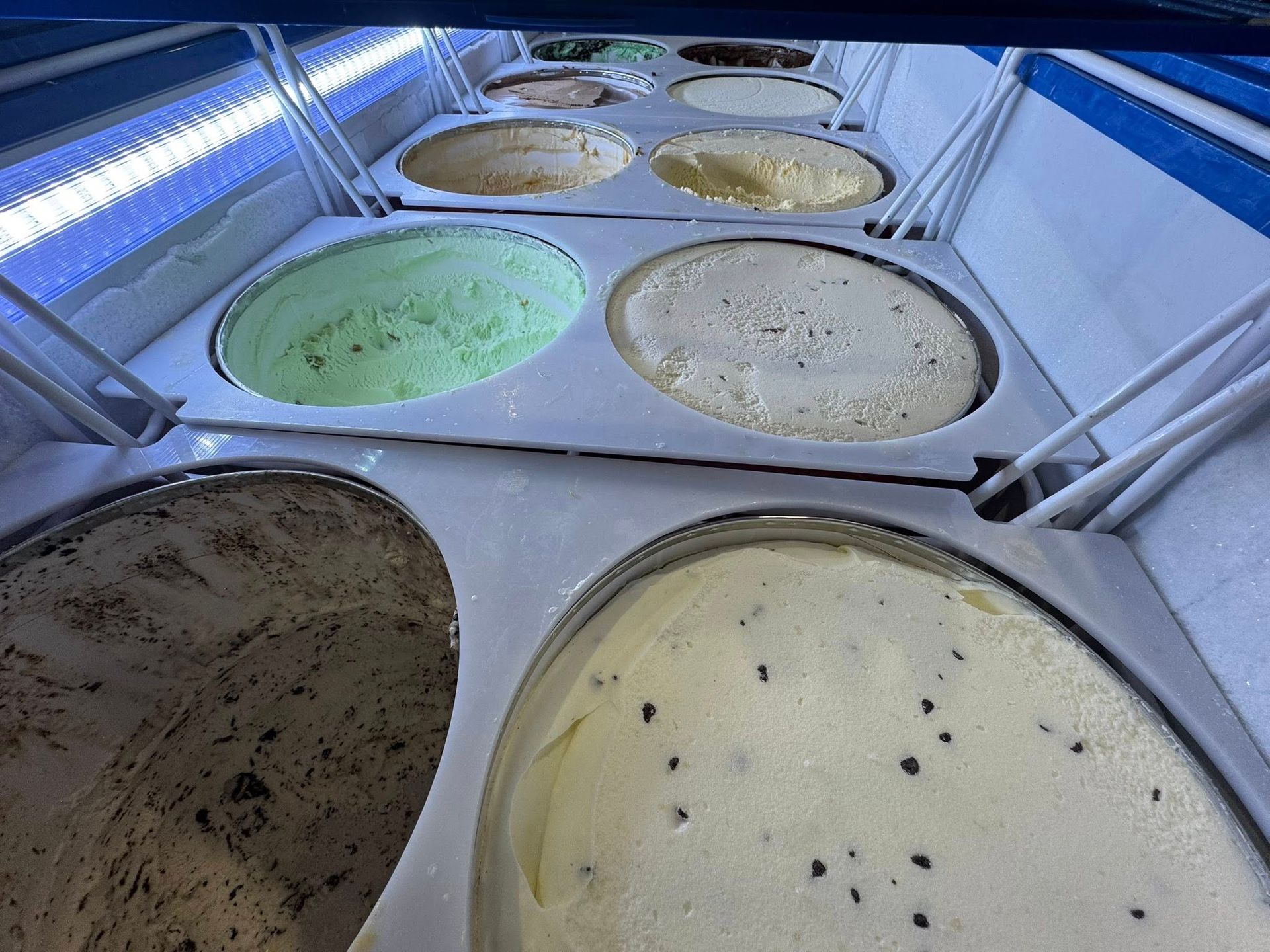 Multiple tubs of assorted ice cream flavors arranged in a refrigerated display case.