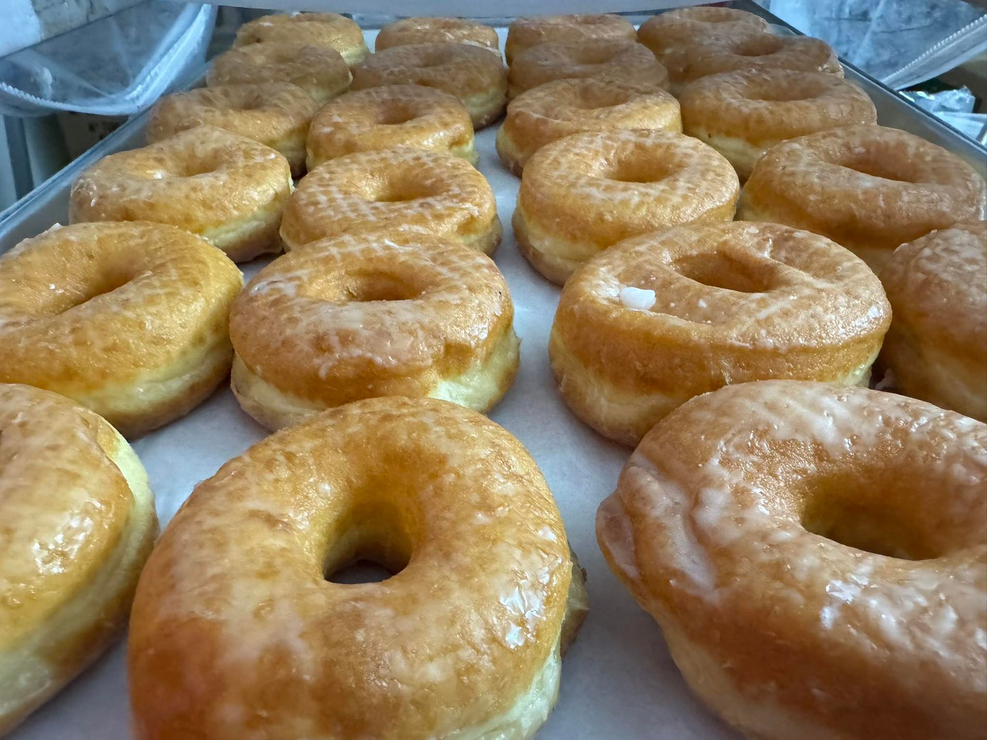 A tray of freshly baked, golden-brown glazed donuts arranged in rows.