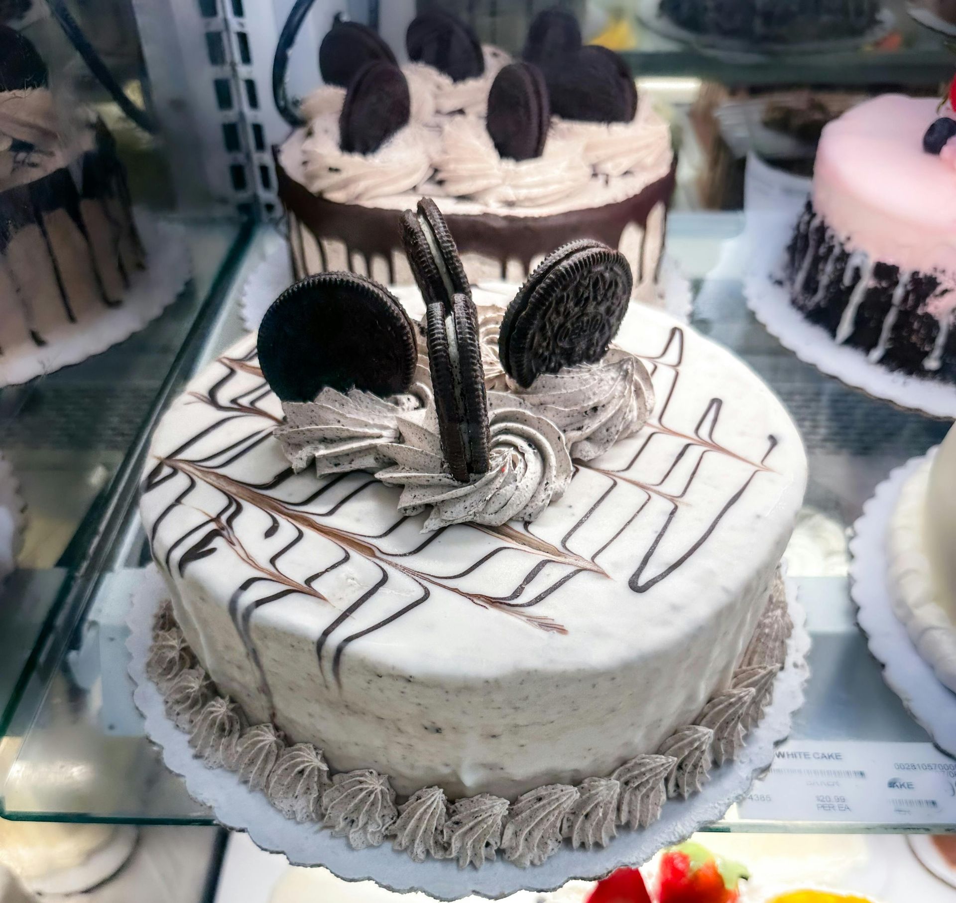 A cookies and cream cake decorated with chocolate drizzle and sandwich cookie halves in a display case.