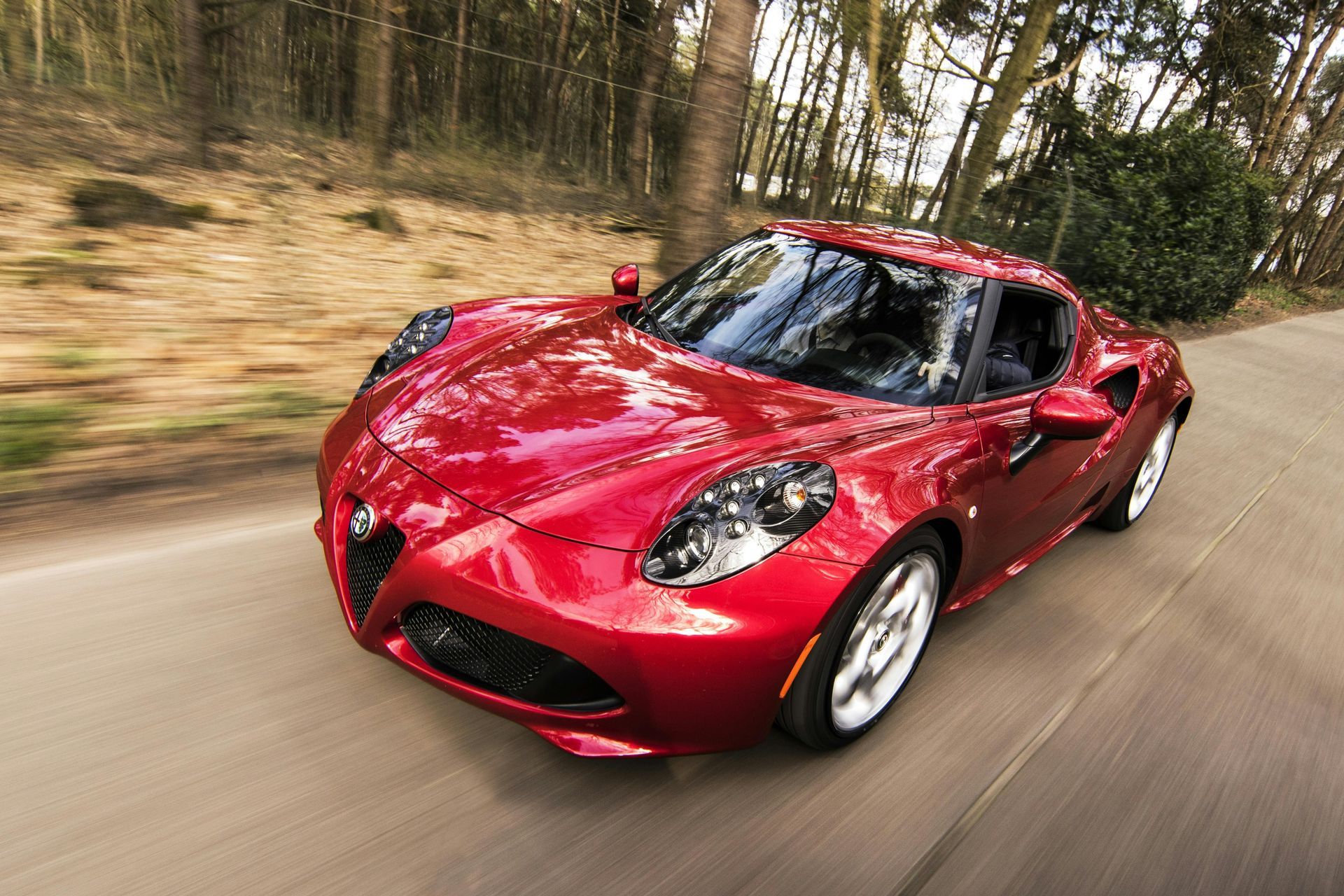 A red sports car is driving down a road in the woods.