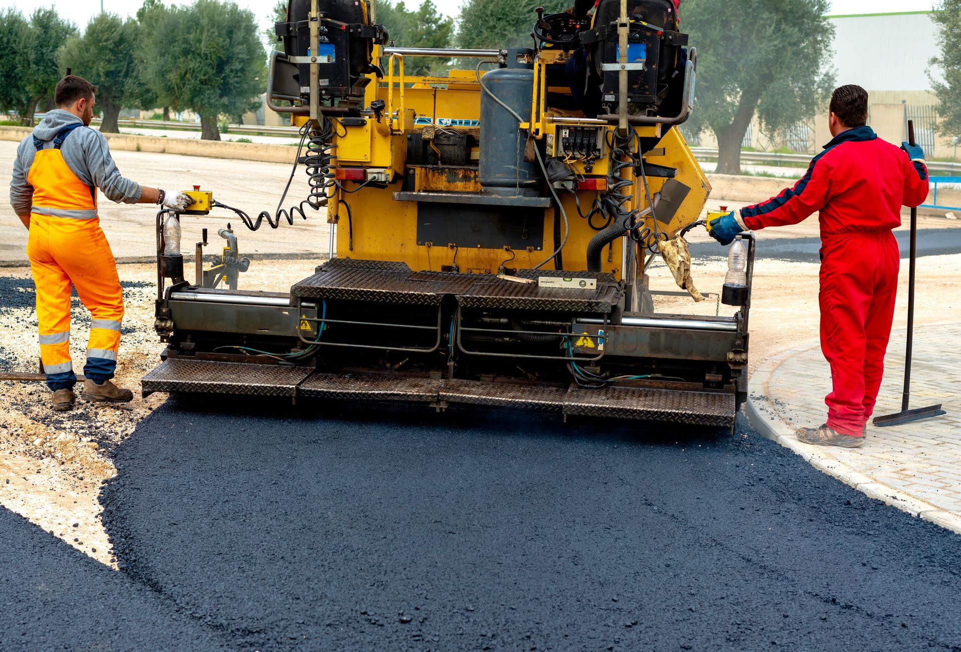 Two men are standing next to a machine that is spreading asphalt