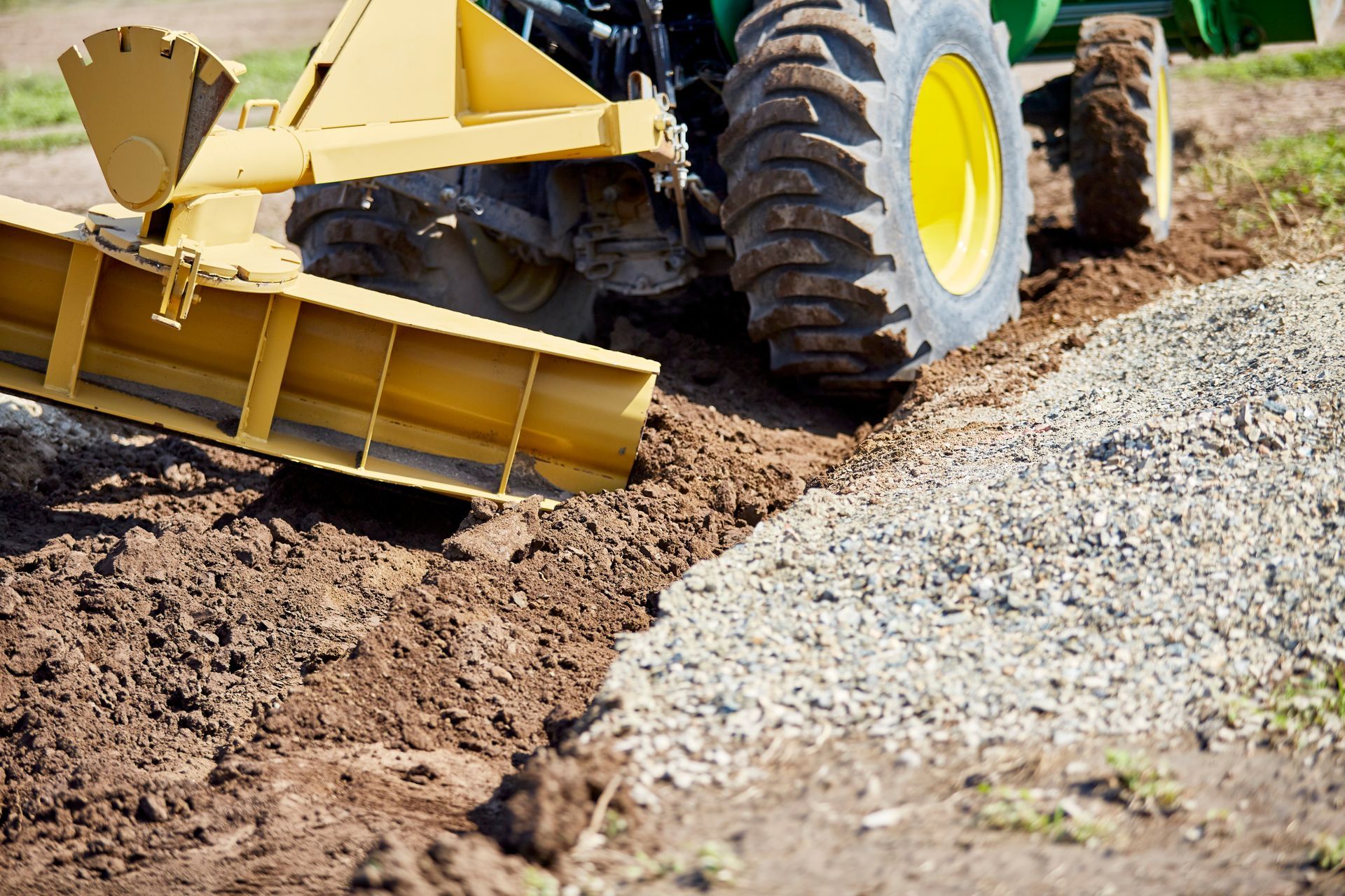 A yellow and green tractor is plowing a dirt road.
