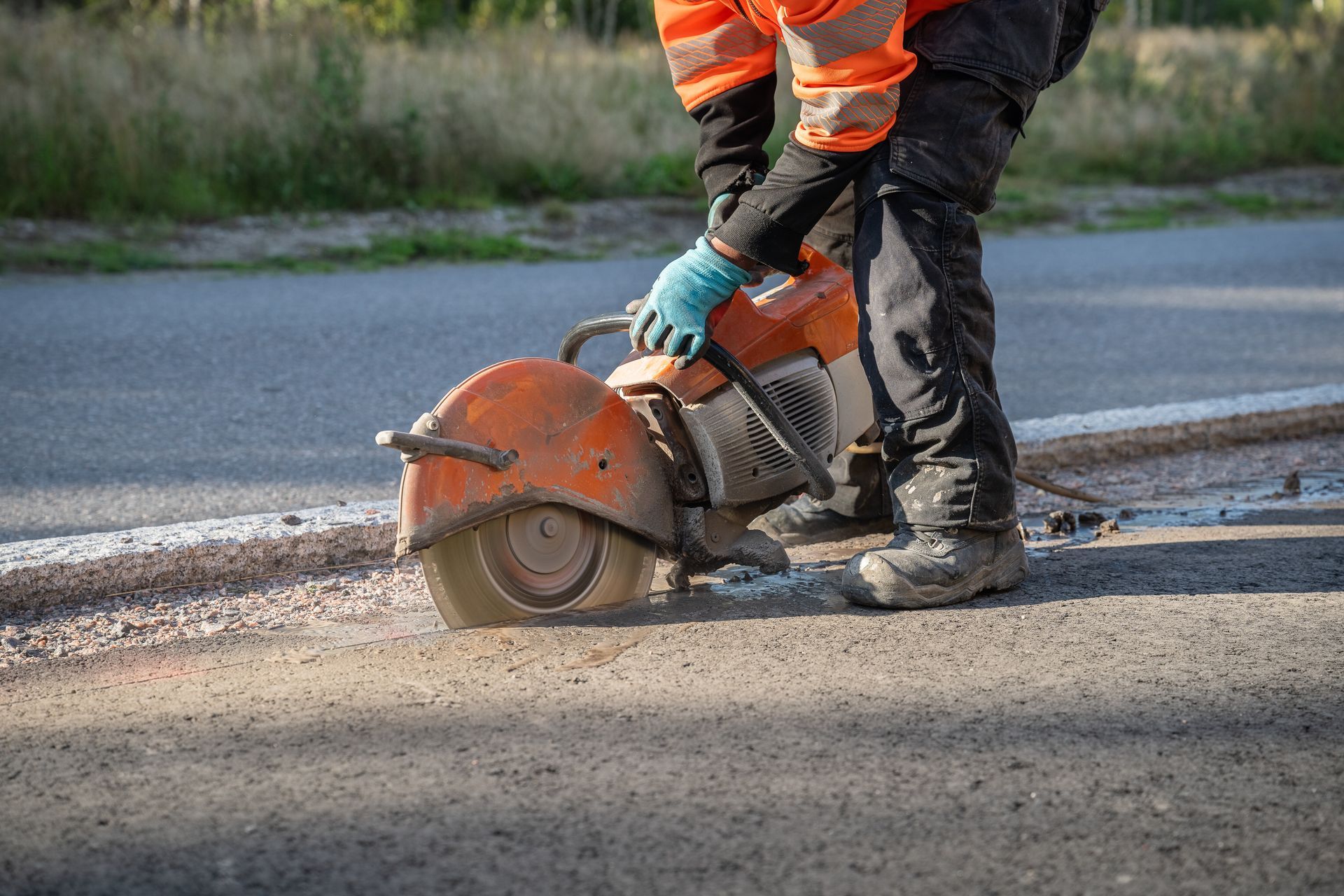 A man is using a circular saw to cut a hole in the road.