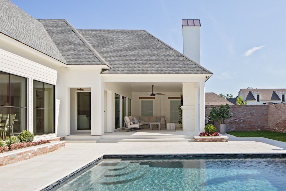 A white modern house with a covered patio, outdoor furniture, and a swimming pool in the foreground under a clear blue sky.