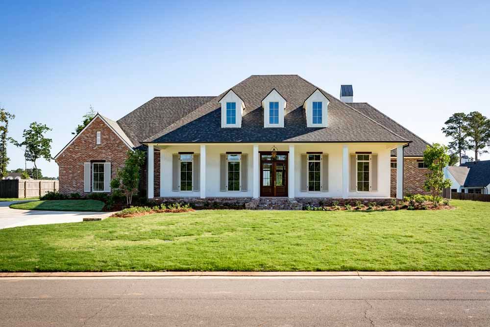 A single-story white house with brick accents, a dark roof, and three front dormers, set behind a large green lawn.
