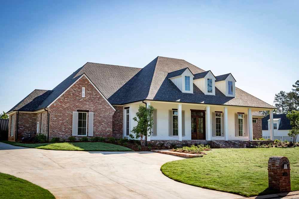 A one-story brick and white house with a dark roof and a spacious front lawn under a clear blue sky.