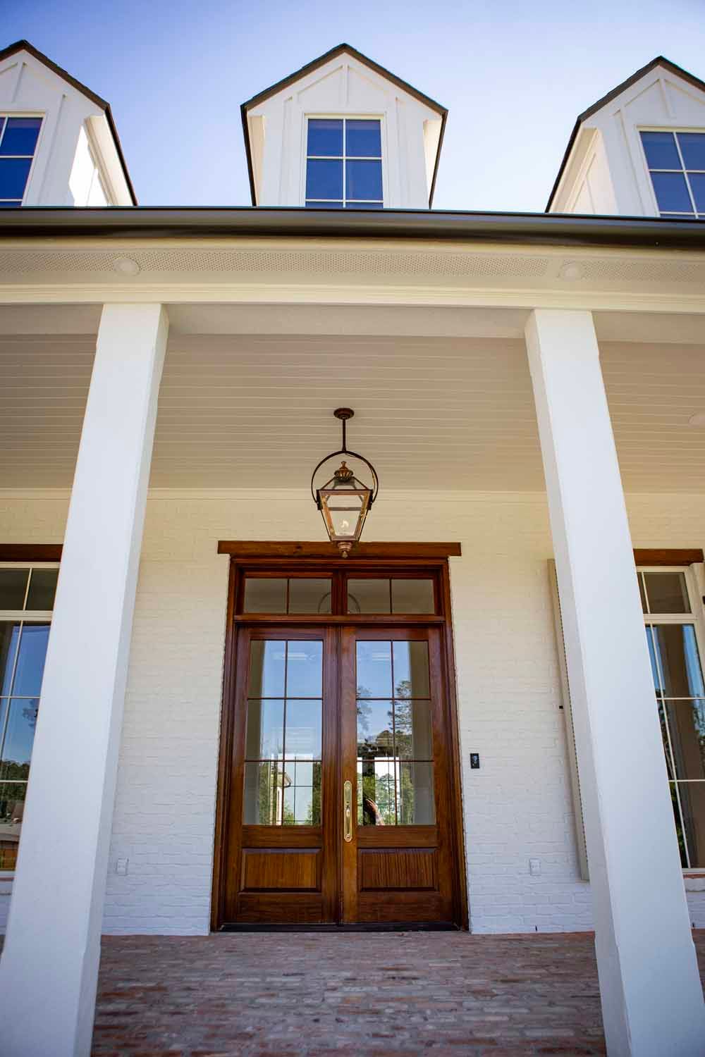 A front porch with a dark wood double door, white brick walls, tall white columns, and three dormer windows above.