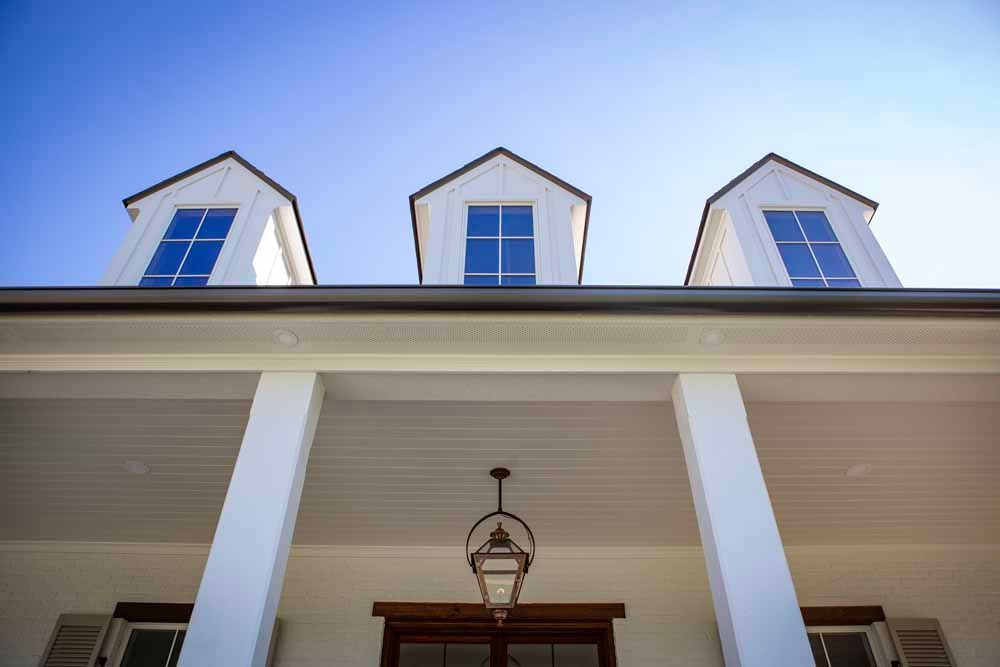 Low-angle view of a white home exterior featuring three symmetrical dormer windows, white pillars, and a hanging lantern.