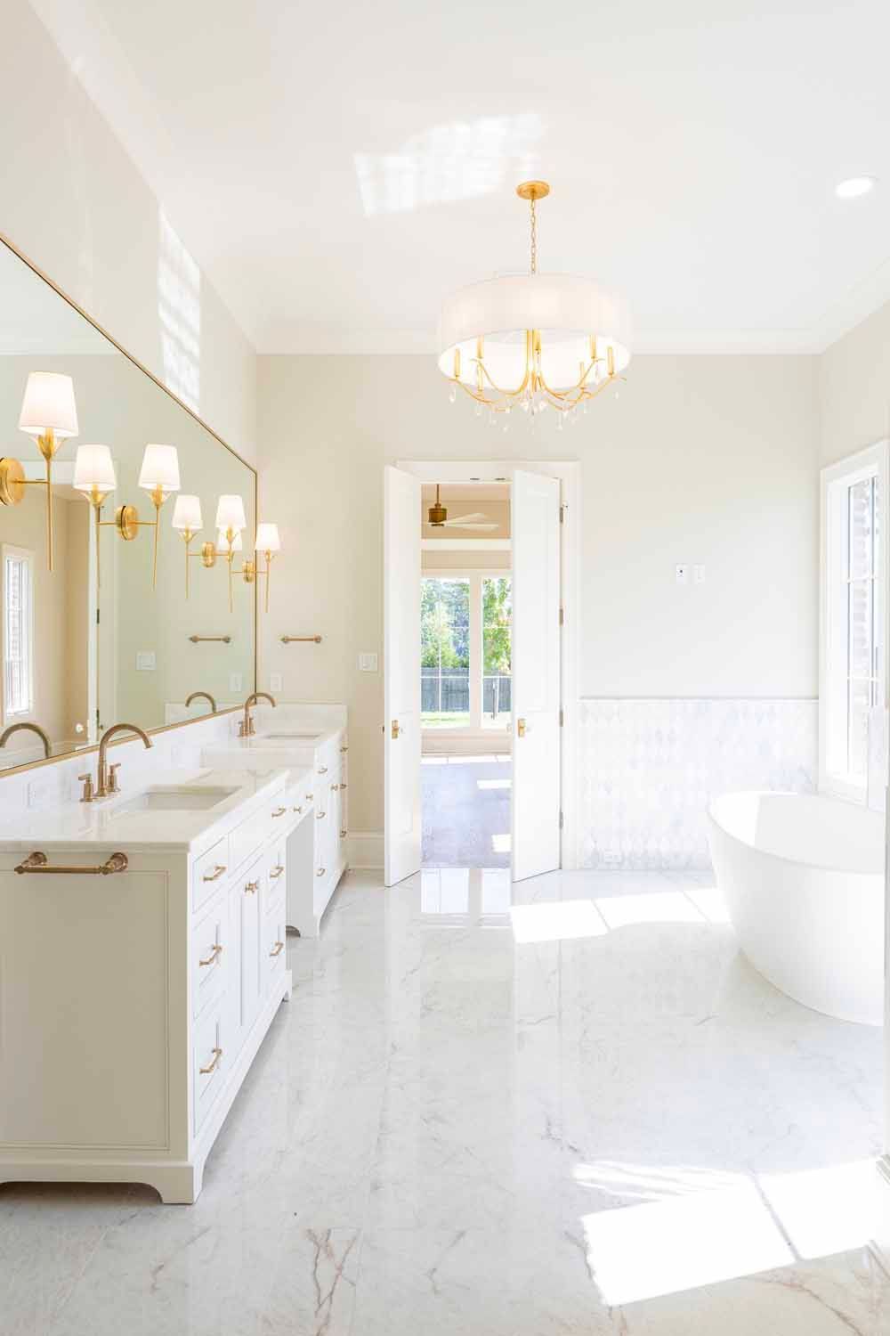 A bright, modern bathroom with a white double vanity, large mirror, elegant chandelier, and a freestanding soaking tub.