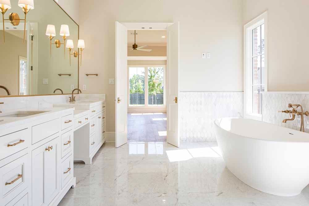 Bright, spacious bathroom with a double white vanity, large mirror, freestanding oval tub, and marble floors.