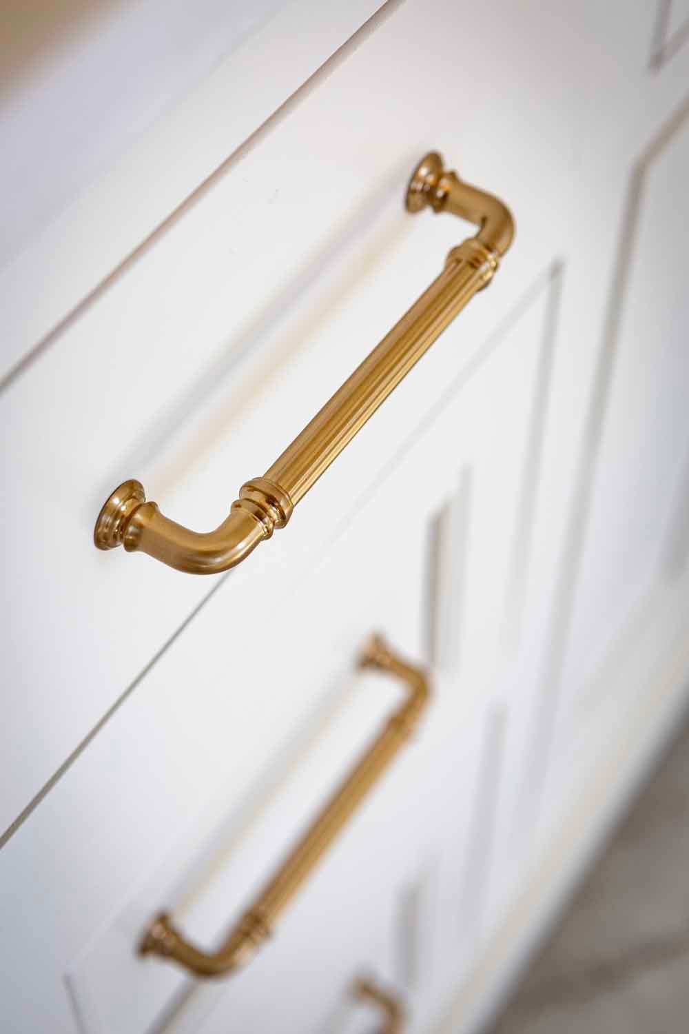 Close-up of white cabinet drawers with ornate gold metal handles.