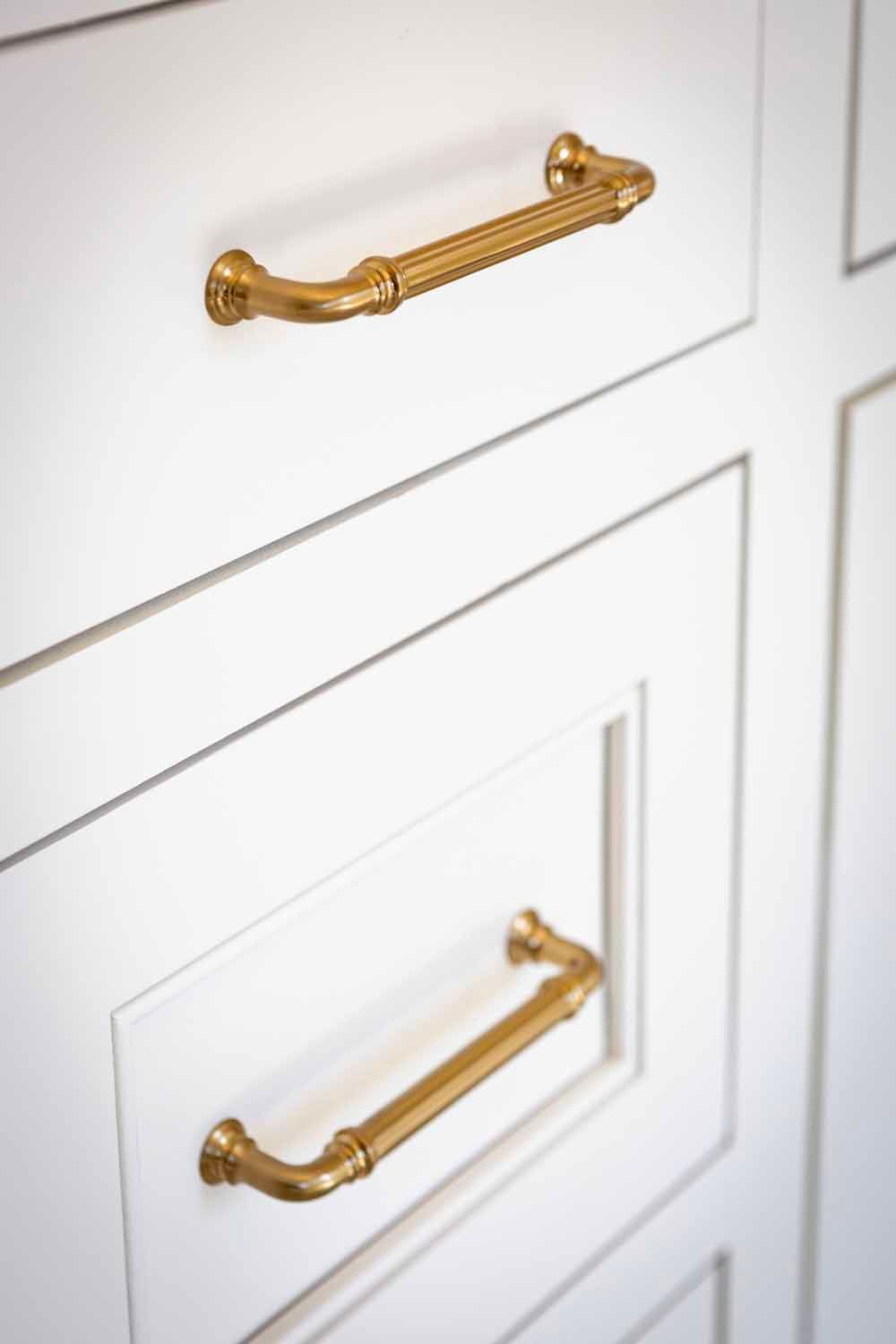 White cabinetry featuring recessed panels with two distinct styles of textured brass drawer pulls.