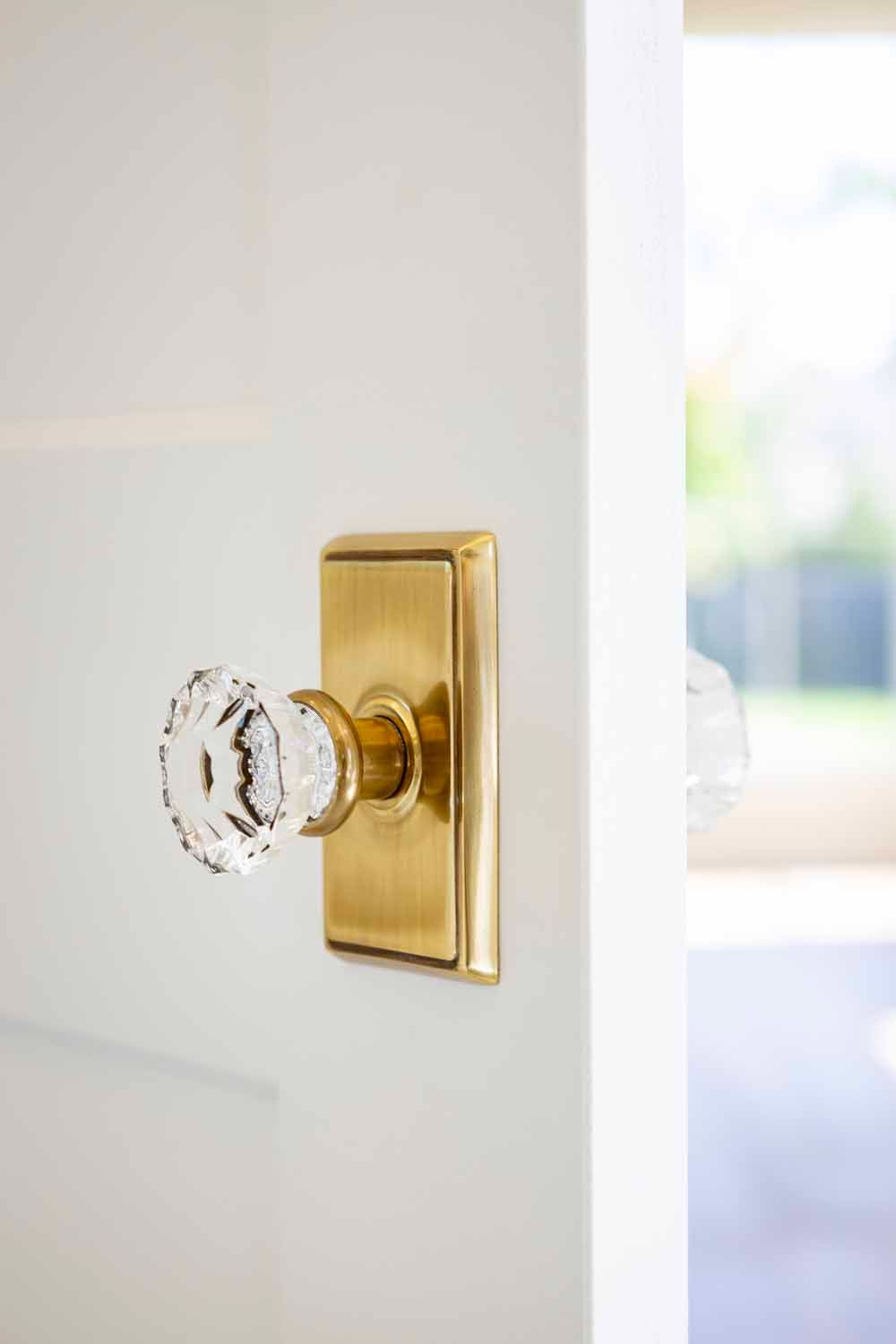 A brass door plate with a faceted crystal knob mounted on a white door.