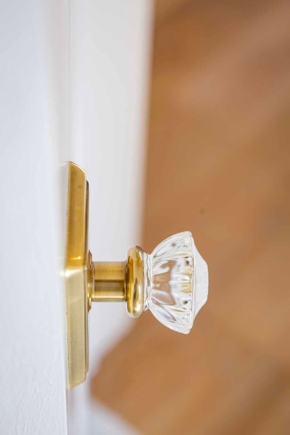 A clear glass crystal doorknob with a polished brass base mounted on a white door.