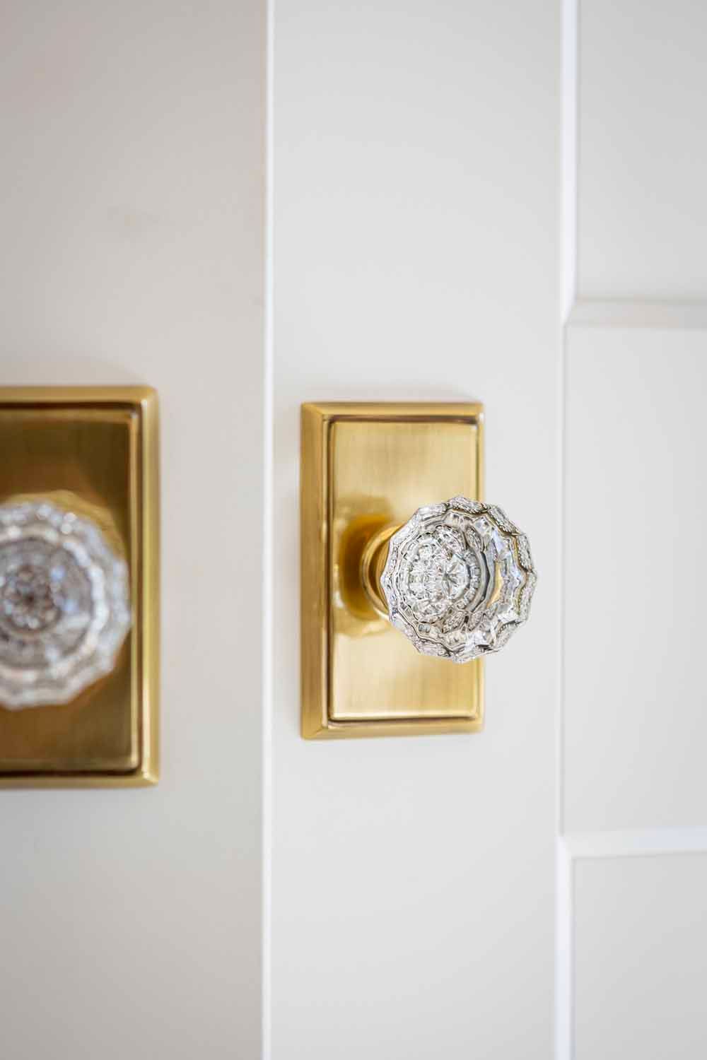 Two vintage-style brass door plates with multifaceted clear glass knobs on a white door.