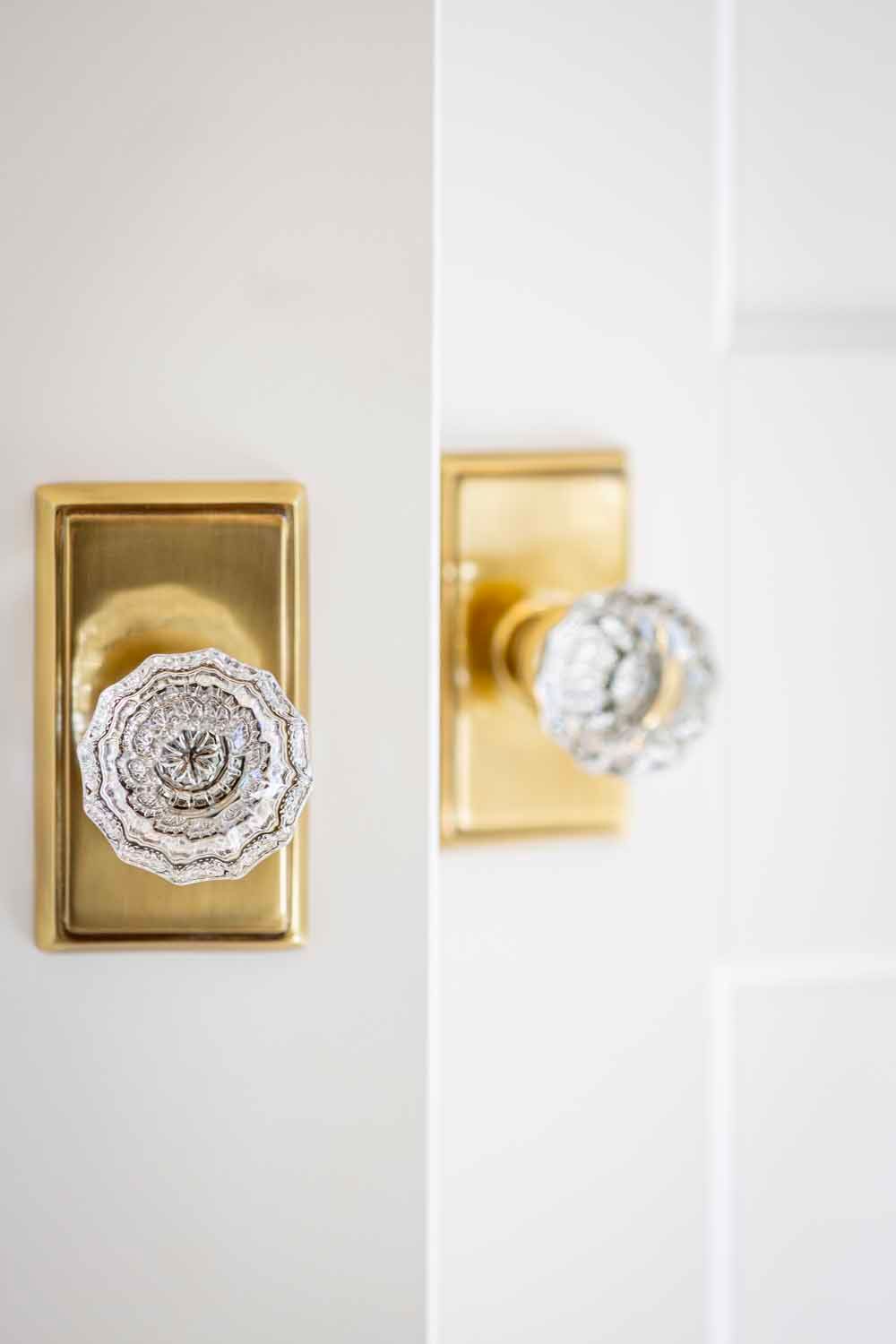 Two brass rectangular door plates with ornate, clear glass crystal knobs mounted on white doors.