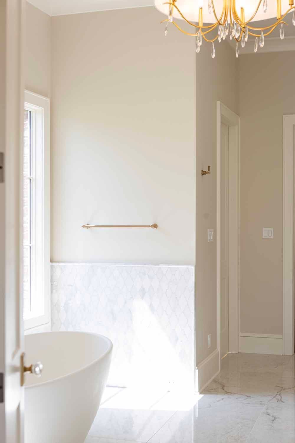 A modern bathroom featuring a white soaking tub, marble flooring, and a gold towel bar on a cream-colored wall.