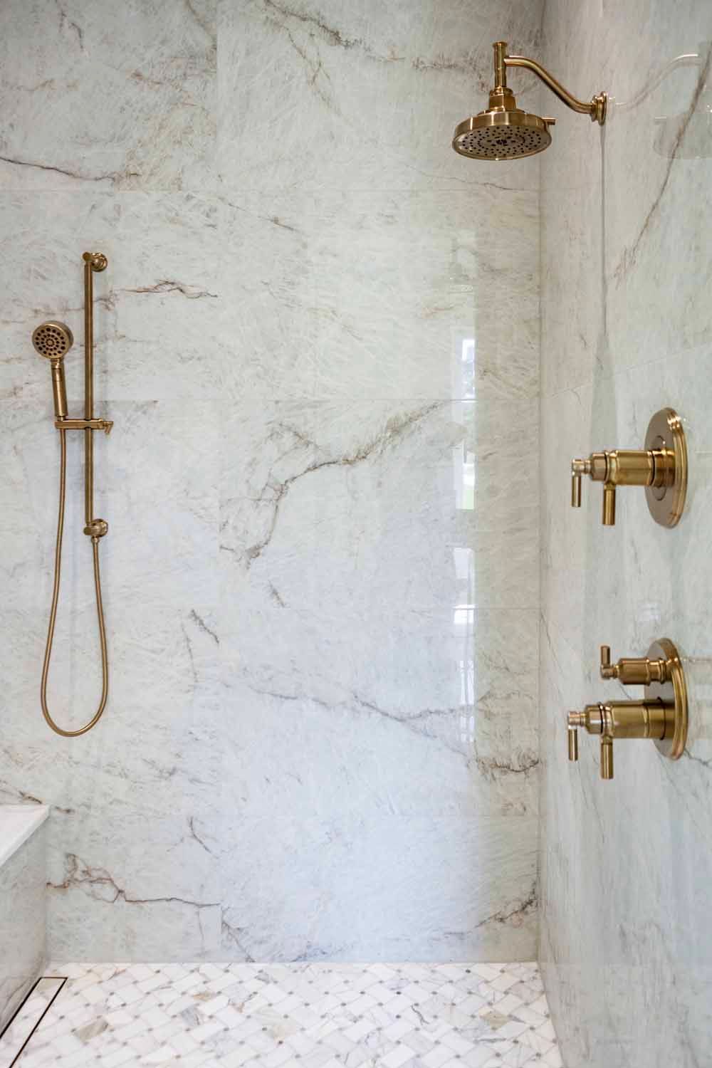 A walk-in shower with white marble walls, gold fixtures, a rainfall showerhead, and a matching handheld sprayer.