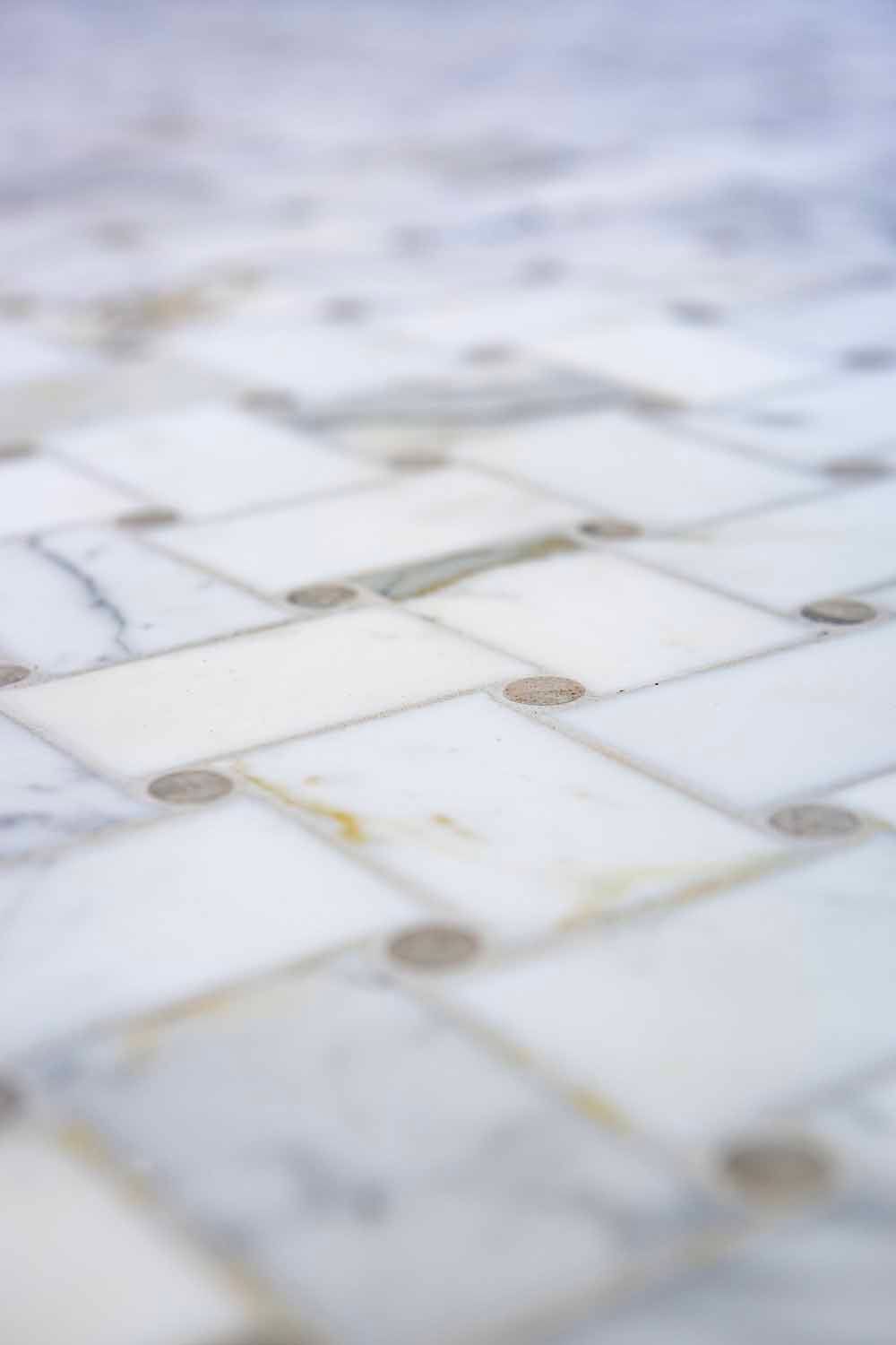 A close-up of a white marble basketweave tile floor with small, circular decorative inserts at the corners.