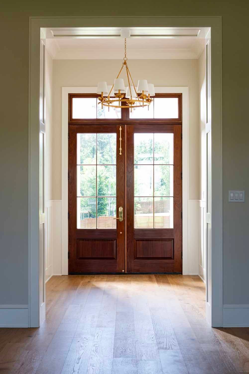 A doorway framed in white trim features a wooden double door with glass panes, illuminated by a gold hanging chandelier.