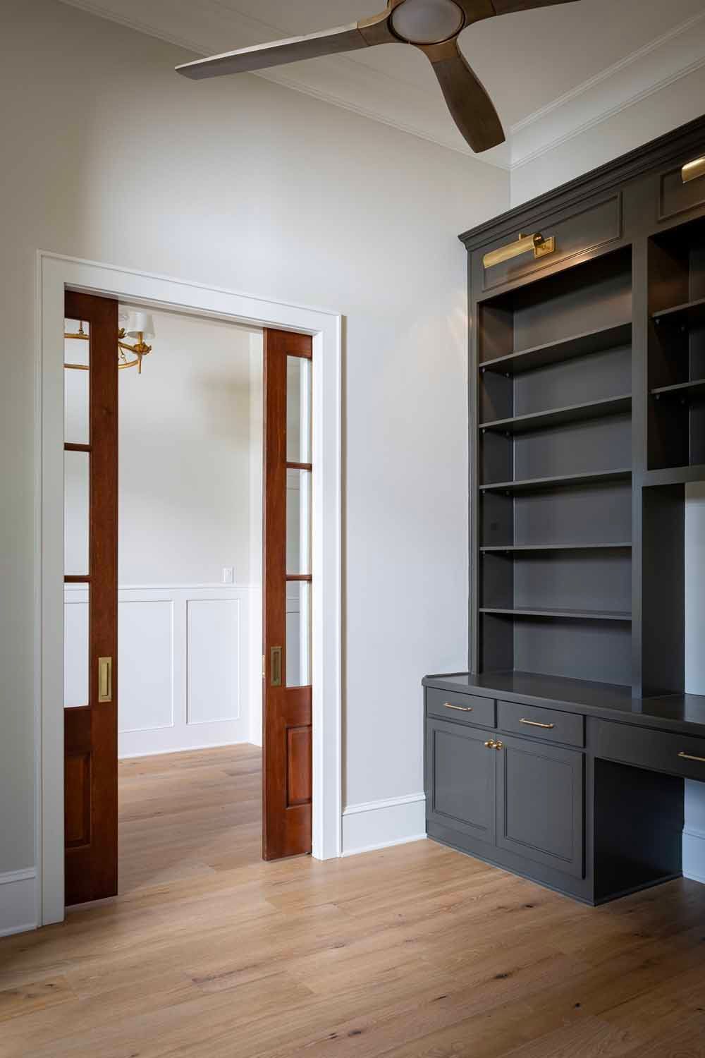 A bright room with light wood floors, a dark built-in desk and bookshelf, and wood-framed glass sliding doors.