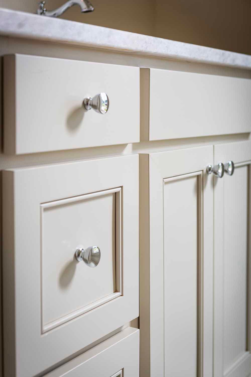 Close-up of cream-colored bathroom vanity cabinets with silver hardware and a marble countertop.