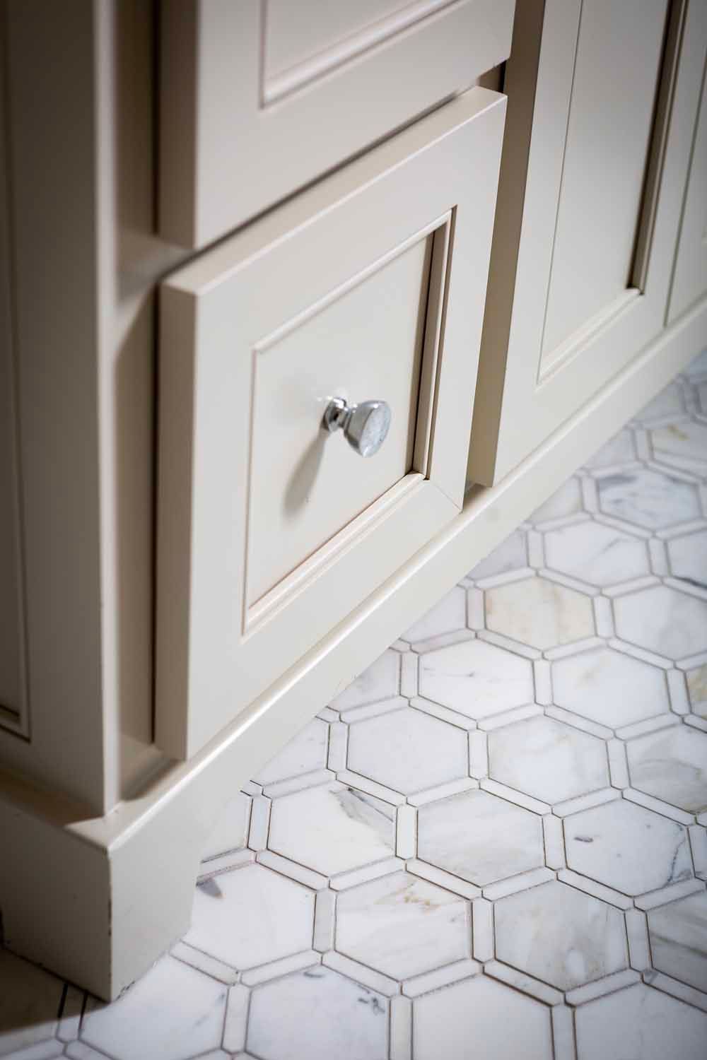 Close-up of a beige cabinet with a silver knob and a marble hexagonal tile floor.