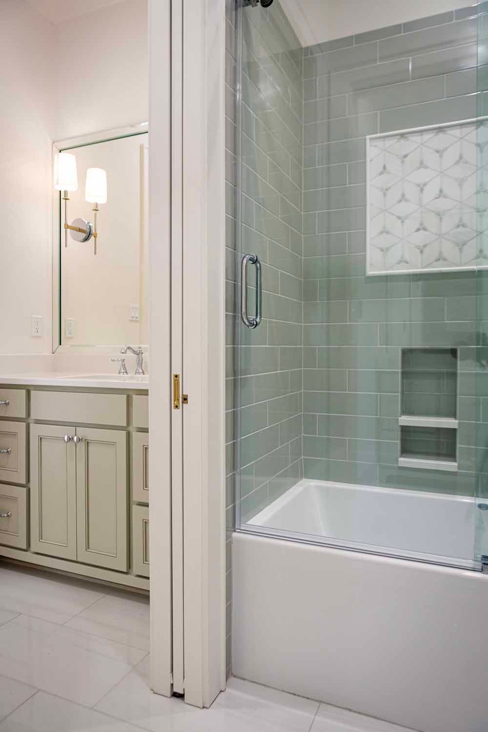 A bathroom featuring a light-colored vanity with a mirror and a glass-enclosed shower with sage green subway tiles.