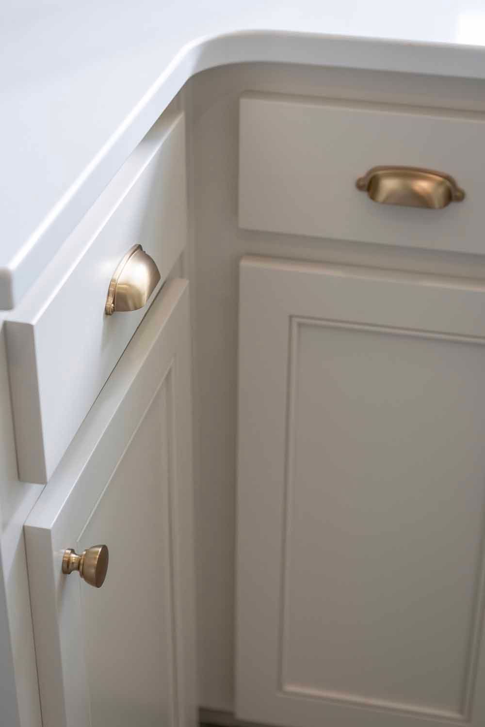Off-white kitchen cabinets with rounded countertops and brushed gold hardware, including cup pulls and a round knob.