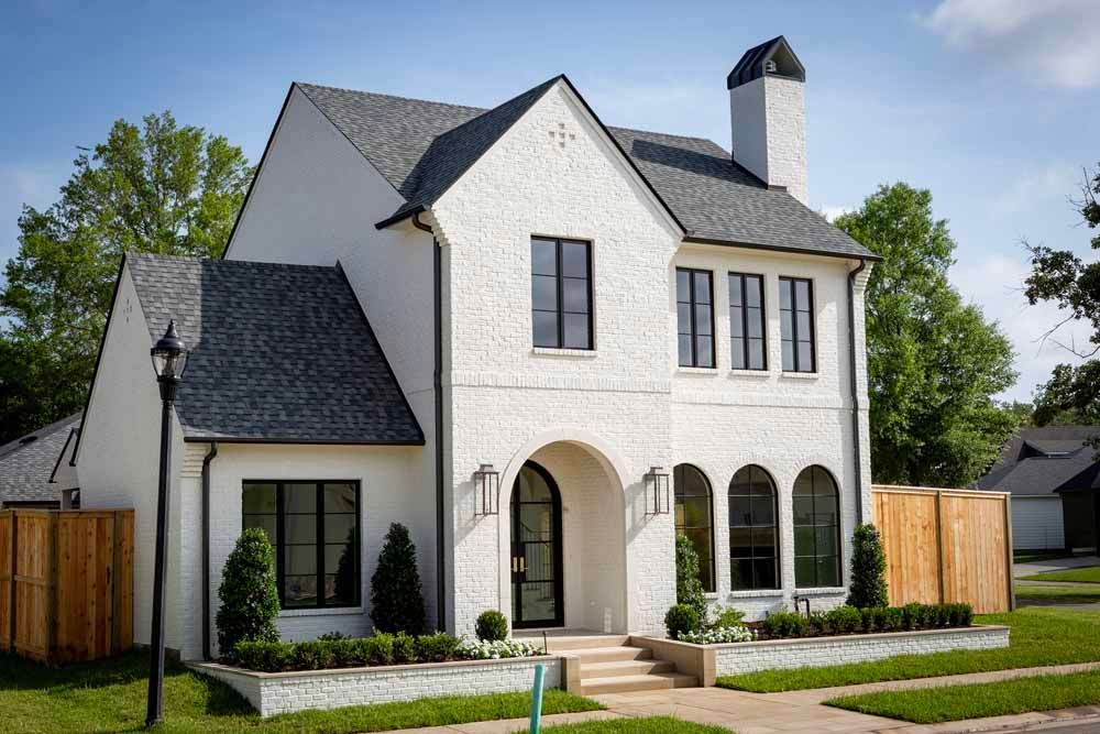 A white brick, two-story house with a grey shingled roof, arched front entry, and black-framed windows.