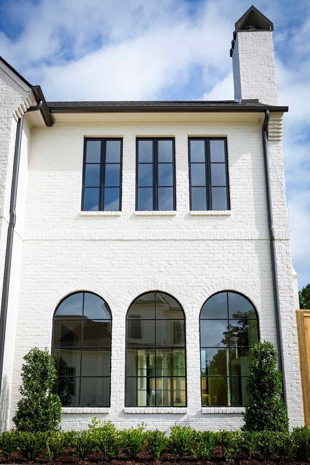 A white brick house exterior with three rectangular upper windows and three arched lower windows, all with black frames.