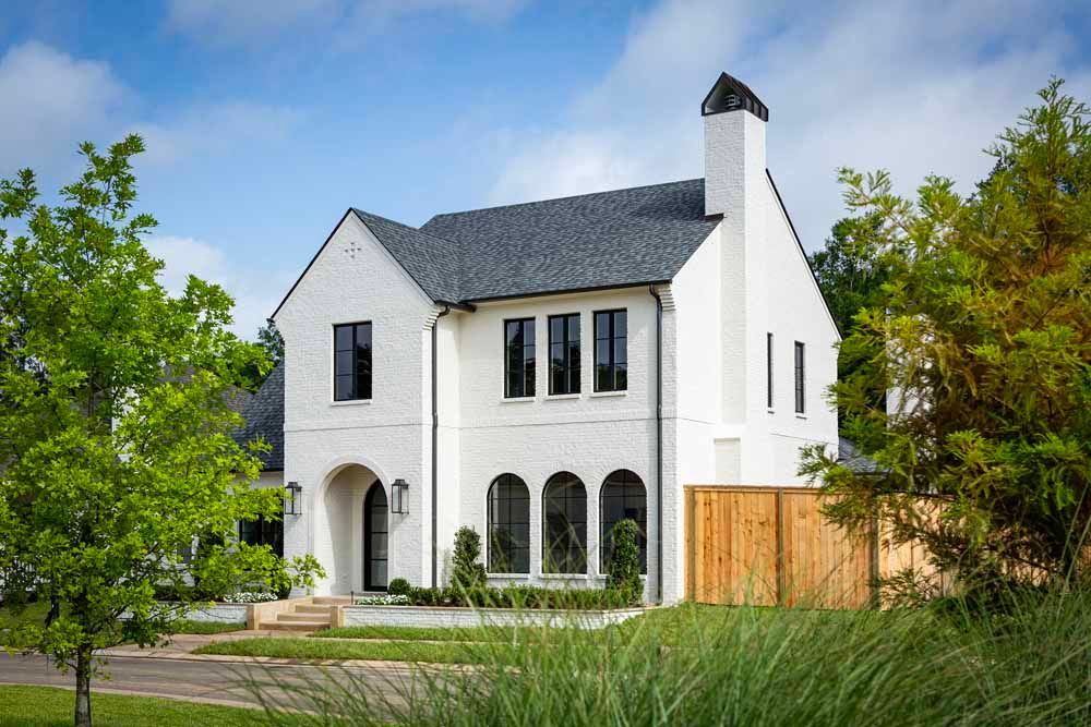 A two-story white brick house with arched ground-floor windows, a dark shingled roof, and a prominent side chimney.