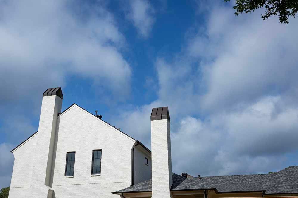 A white house with two prominent, tall chimneys set against a bright blue, cloudy sky.