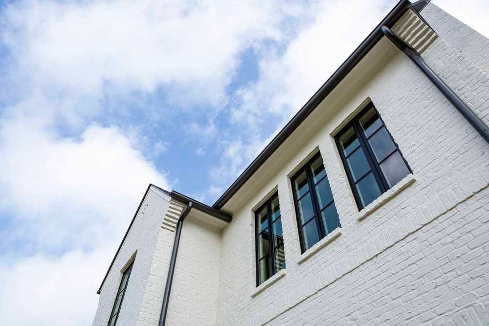 A low-angle view of a white brick building under a blue sky with soft, white clouds.