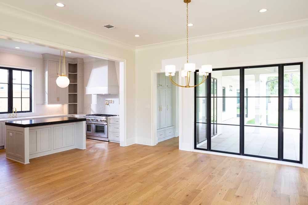 An open-plan room with light hardwood floors, a white kitchen island, and black-framed glass patio doors.