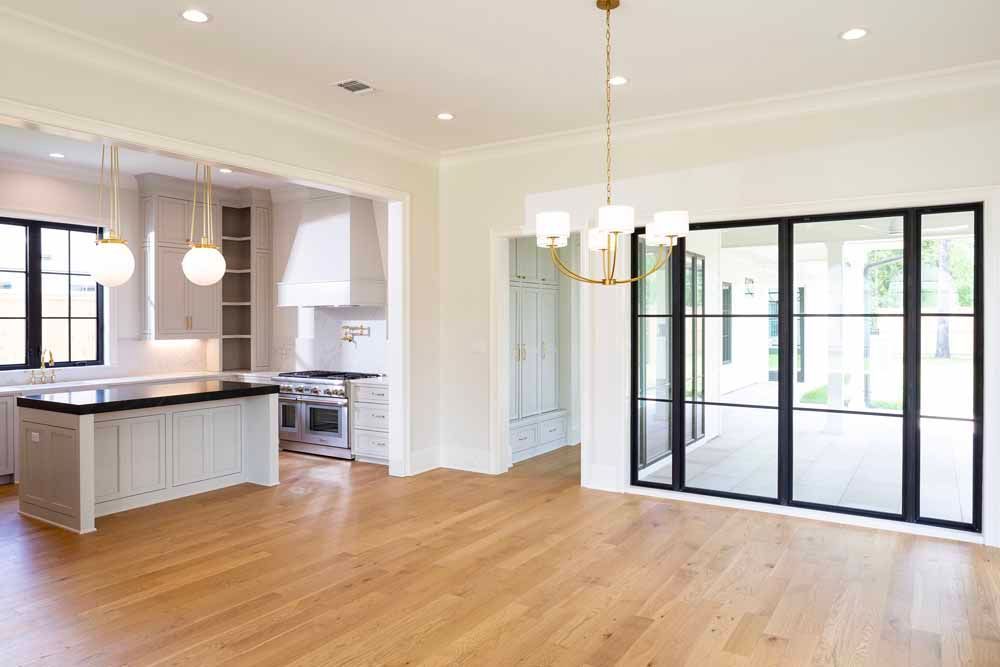 A modern kitchen with light cabinetry and black-framed glass doors looking out to a patio, with light hardwood floors.