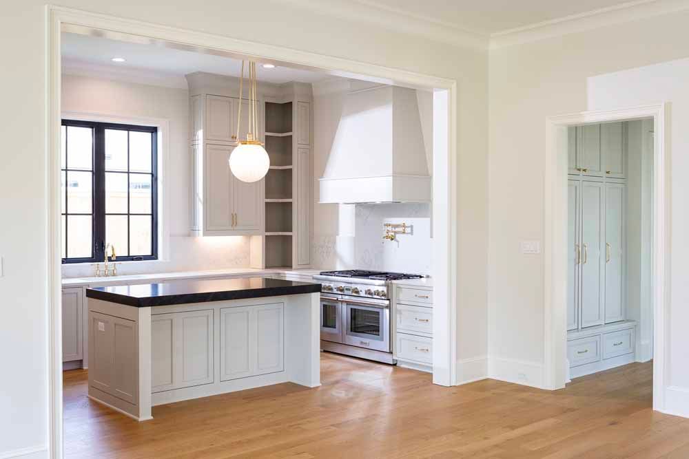 A brightly lit kitchen with a central island, light-colored cabinetry, a large range hood, and light wood flooring.