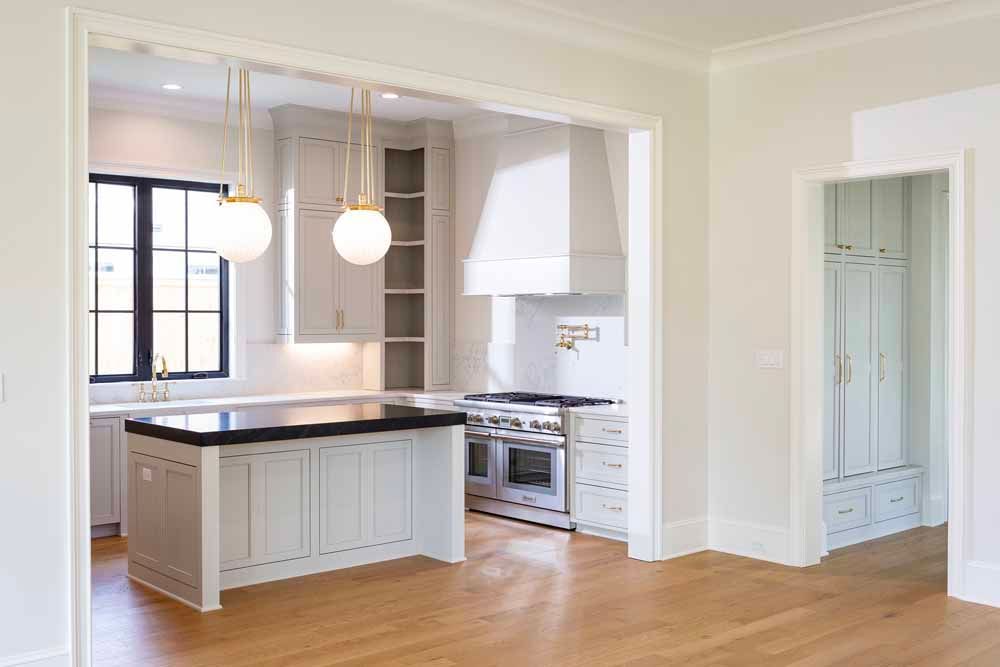 A bright, modern kitchen with a central island, light cabinetry, a stove, and gold globe pendant lighting.