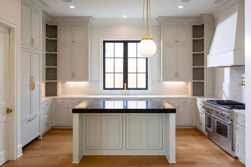 A bright, modern kitchen featuring light gray cabinets, a large island with a black countertop, and a stainless steel stove.